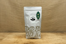 Load image into Gallery viewer, A white stand-up pouch of Chagama tea with a circular white logo and a green decorative label, standing on a wooden surface against a gray wall.