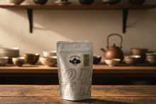 Load image into Gallery viewer, A stand-up pouch of Chagama tea on a wooden surface against a light gray wall. The pouch is white with a circular black and white Chagama logo and a green vertical label with Japanese characters.