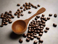 A wooden coffee measuring spoon on a light background.