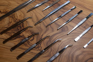 A selection of stainless steel plating tweezers with various tips laid out on a textured surface.